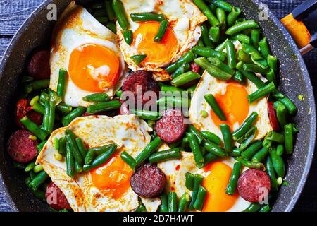 Spanisches Frühstück mit grünen Bohnen gebackenen Eiern und würzigen gebratenen Chorizo-Wurst auf einer Pfanne auf einem Holzhintergrund, Draufsicht, Nahaufnahme Stockfoto