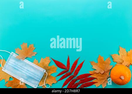 Medizinische Maske zwischen Ahornblättern. Herbstkomposition mit Maske, Ahornblättern und Kürbis. Stockfoto
