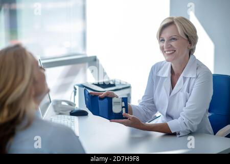 Blonde Ärztin zeigt Blutzuckermessgerät für weibliche Patienten Stockfoto