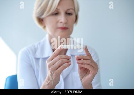 Reife blonde Frau hält Lanzette in ihren Händen, Blick auf sie Stockfoto