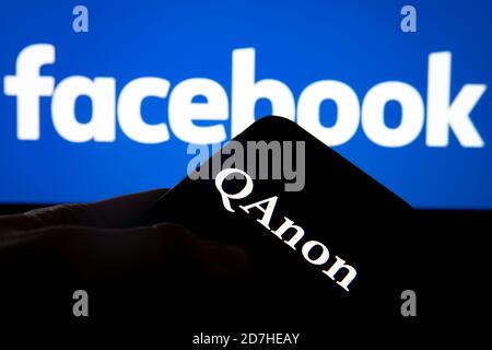 QAnon im Vergleich ZU FACEBOOK. QAnon-Unternehmenslogo auf dem Smartphone, das auf Facebook-Logos platziert ist. Konzept für das Verbot von QAnon in sozialen Medien. Stockfoto