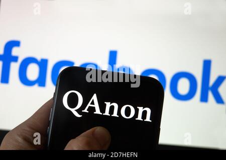 QAnon im Vergleich ZU FACEBOOK. QAnon-Unternehmenslogo auf dem Smartphone, das auf Facebook-Logos platziert ist. Konzept für das Verbot von QAnon in sozialen Medien. Stockfoto