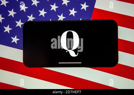 QAnon-Logo auf dem Smartphone, das auf der USA-Flagge platziert ist. Konzept für QAnon oder Q Anon, eine Verschwörungstheorie des tiefen Staates. Stockfoto