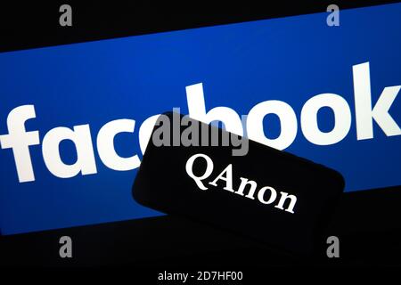 QAnon im Vergleich ZU FACEBOOK. QAnon-Unternehmenslogo auf dem Smartphone, das auf Facebook-Logos platziert ist. Konzept für das Verbot von QAnon in sozialen Medien. Stockfoto