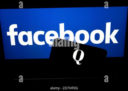 QAnon im Vergleich ZU FACEBOOK. QAnon-Unternehmenslogo auf dem Smartphone, das auf Facebook-Logos platziert ist. Konzept für das Verbot von QAnon in sozialen Medien. Stockfoto