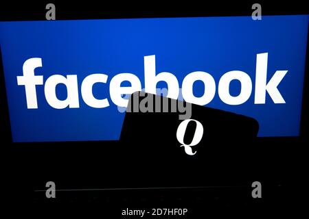 QAnon im Vergleich ZU FACEBOOK. QAnon-Unternehmenslogo auf dem Smartphone, das auf Facebook-Logos platziert ist. Konzept für das Verbot von QAnon in sozialen Medien. Stockfoto