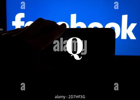 QAnon im Vergleich ZU FACEBOOK. QAnon-Unternehmenslogo auf dem Smartphone, das auf Facebook-Logos platziert ist. Konzept für das Verbot von QAnon in sozialen Medien. Stockfoto