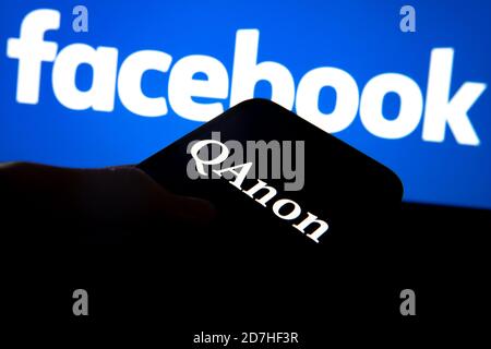 QAnon im Vergleich ZU FACEBOOK. QAnon-Unternehmenslogo auf dem Smartphone, das auf Facebook-Logos platziert ist. Konzept für das Verbot von QAnon in sozialen Medien. Stockfoto
