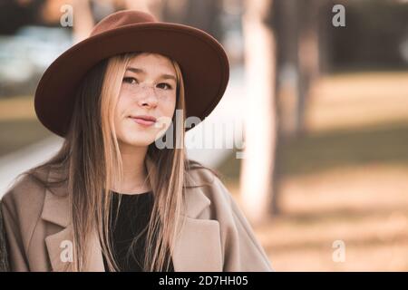 Schöne blonde Teenager-Mädchen 13-14 Jahre alt trägt Hut und Jacke im Park im Freien. Blick auf die Kamera. Teenagerhood. Herbstsaison. Stockfoto