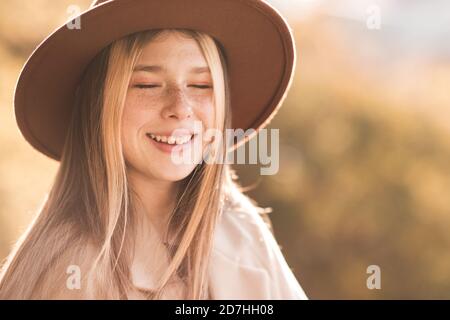 Lachen glücklich Teenager-Mädchen 13-14 Jahre alt mit geschlossenen Augen tragen stilvolle Hut und Mantel über Natur Herbst Hintergrund Nahaufnahme. Glück. Teenagerho Stockfoto