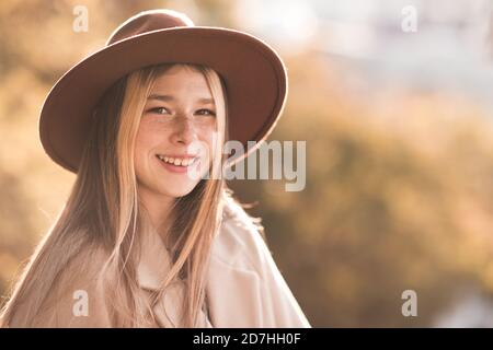 Lächelndes Teenager-Mädchen 13-14 Jahre alt trägt Hut und Mantel über Herbst Natur Hintergrund Nahaufnahme. Blick auf die Kamera. Teenagerhood. Glück. Stockfoto