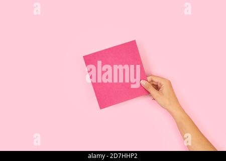 Frau Hand hält ein leeres rosa Papier auf einem rosa Hintergrund Stockfoto