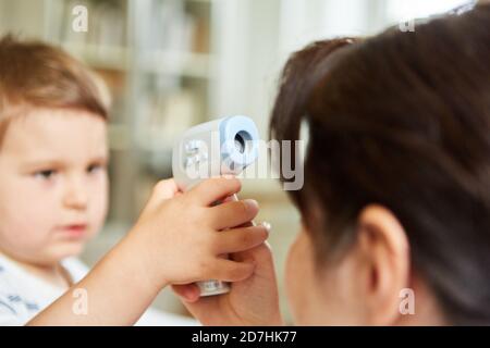 Kind und Kinderarzt üben die Messung von Fieber mit dem berührungslosen Infrarot Stirnthermometer Stockfoto