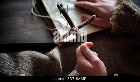 Religiöse altes Buch auf einem Holztisch. Eine religiöse Kreuz mit einem Seil und Sackleinen, neben der Bibel gebunden. Gottesdienst, Sünden und das Gebet. Stockfoto