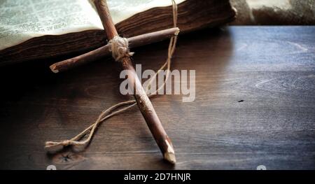 Religiöse altes Buch auf einem Holztisch. Eine religiöse Kreuz mit einem Seil und Sackleinen, neben der Bibel gebunden. Gottesdienst, Sünden und das Gebet. Stockfoto