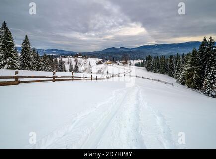 Sekundäre Landschaft alpine Straße in abgelegenen Bergdorf, Schneeverwehungen und Holzzaun am Wegesrand Stockfoto