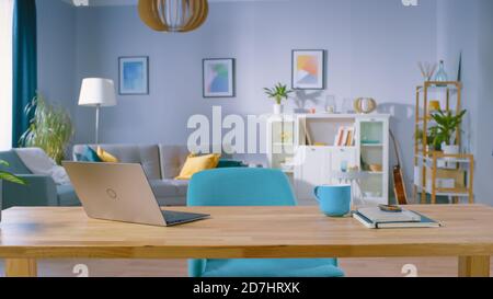 Stilvolles Interieur des Wohnzimmers mit Holzschreibtisch mit Laptop, stilvollen Stühlen, Sofa. Geschmackvolle, farbenfrohe Möbel in Serene-Tönen Stockfoto