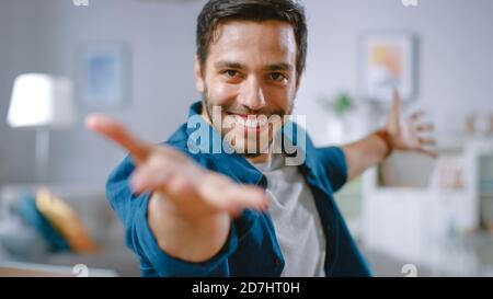 Schöner glücklicher Mann macht lustige Tanzroutine, während er an seinem Schreibtisch im Wohnzimmer sitzt. Stockfoto