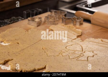 Weihnachtsbäckerei: Plätzchenteig (Mürbeteig) ausgerollt. Verschiedene Cookie-Formen ausgeschnitten. Nudelholz und Ausstechformen im Hintergrund; selektiv f Stockfoto