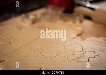 Weihnachtsbäckerei: Plätzchenteig (Mürbeteig) ausgerollt. Verschiedene Cookie-Formen ausgeschnitten. Nudelholz und Ausstechformen im Hintergrund; selektiv f Stockfoto