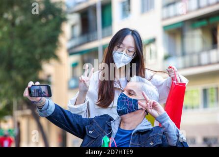 Begeistert multiethnischen Freunde tragen Schutzmasken unter Selfie auf dem Smartphone Beim Zeigen V-Schild und genießen Spaziergang während Coronavirus epidemii Stockfoto