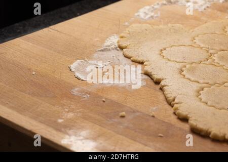 Weihnachtsbacken: Plätzchenteig (Mürbeteig) auf einem hölzernen Küchenteller auf Mehl ausgerollt. Runde Kekse ausgeschnitten. Selektiver Fokus. Stockfoto