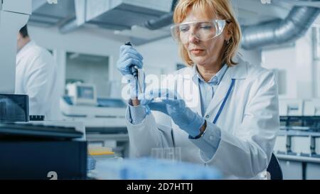 Forscherin verwendet Mikropipette, während sie mit Teströhrchen arbeitet. Menschen im innovativen pharmazeutischen Labor mit moderner Medizin Stockfoto