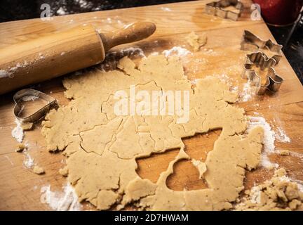 Plätzchenteig (Mürbeteig) auf Mehl auf einem hölzernen Küchentafel auf schwarzer Theke ausgerollt. Nudelholz und Ausstechformen sichtbar. Verschiedene Cookies c Stockfoto