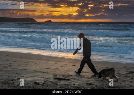 Ein spektakulärer Sonnenuntergang, wenn ein Mann seinen Hund am Fistral Beach in Newquay in Cornwall spaziert. Stockfoto