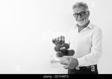 Studio shot von Happy älterer bärtiger Mann lächelnd, während sie Geschenkbox und Teddybär mit Herz und Liebe Zeichen gegen weißen Hintergrund Stockfoto