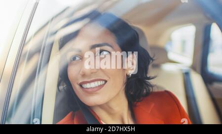 Beautiful Happy Woman fährt auf einem Beifahrersitz eines Autos, schaut in Wonder auf Big City View. Kamera außerhalb des fahrenden Autos montiert. Stockfoto