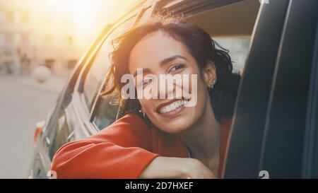 Happy Beautiful Woman Riding on a Back Seat of a Car, blickt aus dem offenen Fenster in Wonder. Travelling Girl Erleben Sie Magie der Welt. Sunny Shot Stockfoto