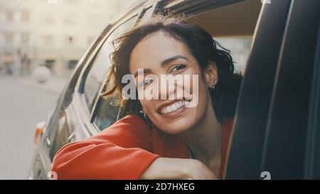 Happy Beautiful Woman Riding on a Back Seat of a Car, blickt aus dem offenen Fenster in Wonder of the Big City. Travelling Girl Erleben Sie die Magie der Stockfoto