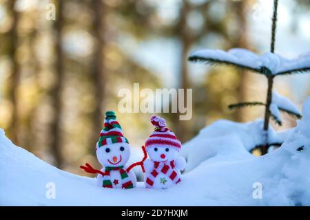 Zwei kleine lustige Spielzeug baby Schneemann auf gestrickte Mützen und Schals in tiefem Schnee im Freien in der Nähe von Pine Tree Branch. Frohes Neues Jahr und Frohe Weihnachten Gruß Stockfoto