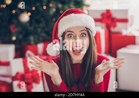 Foto von schockiert junge Mädchen Geschenke Hände öffnen Mund starren Tragen sie weihnachtsmann Kopfbedeckung roten Pullover im dekorierten Weihnachten Wohnzimmer In Innenräumen Stockfoto