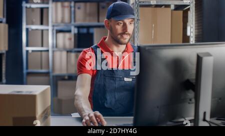 Porträt eines uniformierten Arbeiters, der einen Computer benutzt, während er an seinem Schreibtisch im Lager sitzt. Stockfoto