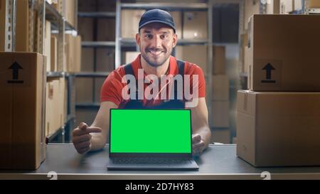 Happy Worker Punkte bei Laptop, zeigt Daumen hoch und Notebook mit grünem Mock-up-Bildschirm. Stockfoto