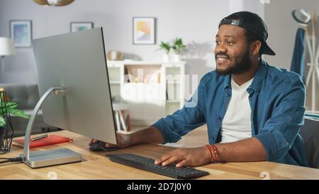 Portrait des stylischen Afroamerikaners, der an einem PC arbeitet, während er zu Hause an seinem Schreibtisch sitzt. Stockfoto