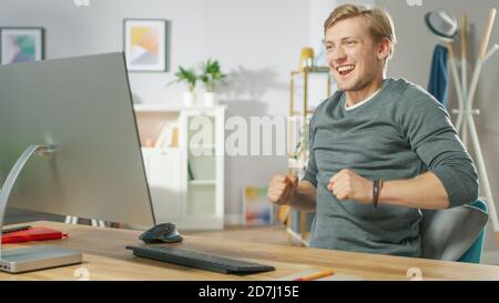 Porträt des hübschen jungen Mannes tanzt, während er vor seinem Computer sitzt. Junger Mann mit Spaß zu Hause. Stockfoto