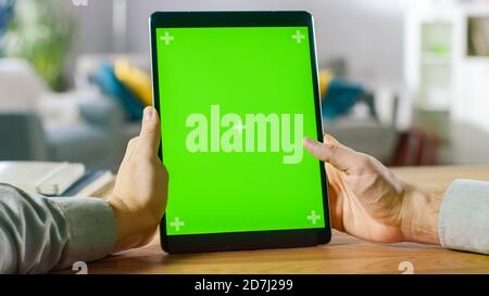 Nahaufnahme eines Mannes Hand hält Green Mock-up-Bildschirm Smartphone. Modernes Mobiltelefon. Im Hintergrund gemütliches Wohnzimmer oder Home Office. Stockfoto