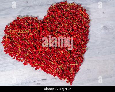 Die roten Johannisbeeren wurden aus dem Busch gezupft und in Form eines Herzens in einem Haufen aufgestapelt. Stockfoto