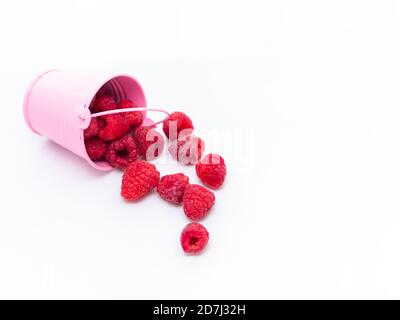 Rote reife Himbeeren fallen aus einem rosa Eimer auf weißem Hintergrund. Stockfoto