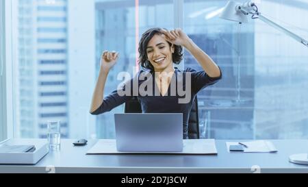 Porträt der schönen Geschäftsfrau tanzend, während sie an ihrem Schreibtisch sitzt. Erfolgreiche und glückliche Frau feiert Rekordverkäufe. Stockfoto