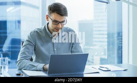Erfolgreicher junger Geschäftsmann arbeitet in seinem Modern Office auf einem Laptop. Intelligenter junger Mann, der für einen vielversprechenden neuen Startpup arbeitet. Stockfoto