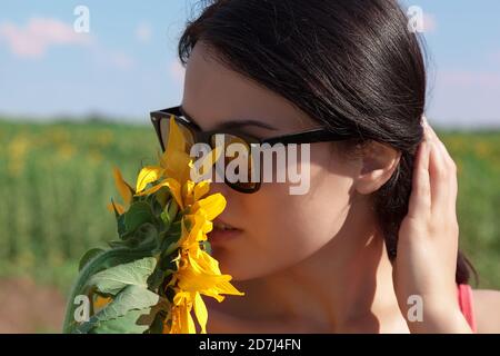 Schönes Mädchen mit Sonnenbrille auf einem Feld mit Sonnenblumen an einem sonnigen Sommertag. Stockfoto