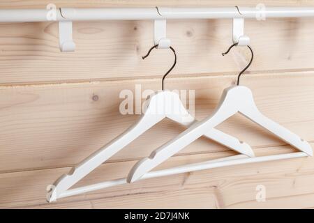 Zwei weiße Kleiderbügel befinden sich in der Nähe einer leeren Holzwand, Nahaufnahme Stockfoto
