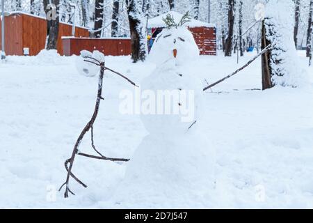 Schneemann in einem Stadtpark mit Bäumen und Konstruktionen im Hintergrund. Traditionelles Wintervergnügen. Stockfoto