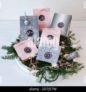 Adventskalender mit Paket auf einem weißen Holztablett, im Hintergrund ein Krug mit Kiefernästen bei warmem Kerzenlicht Stockfoto