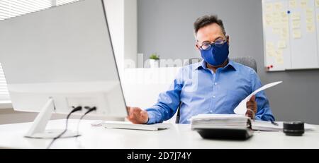 Ältester Geschäftsangestellte, Der Bei Computer Wearing Facial Mask Arbeitet Stockfoto