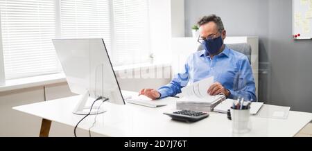 Ältester Geschäftsangestellte, Der Bei Computer Wearing Facial Mask Arbeitet Stockfoto